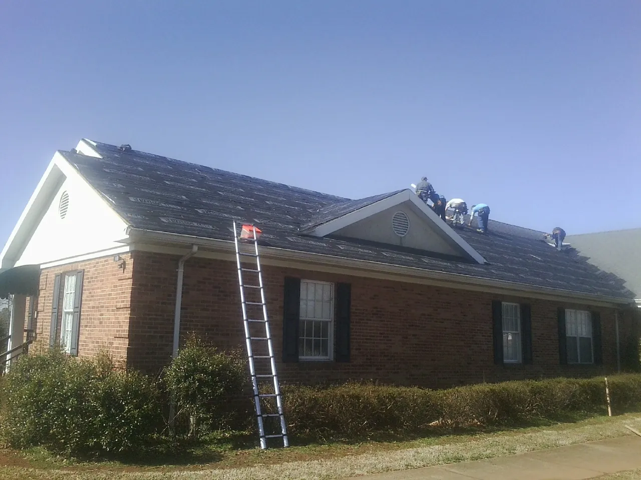 Crew tearing shingles off a brick ranch roof with a ladder set — Metal Roof Repair work by our crew in Mattapoisett