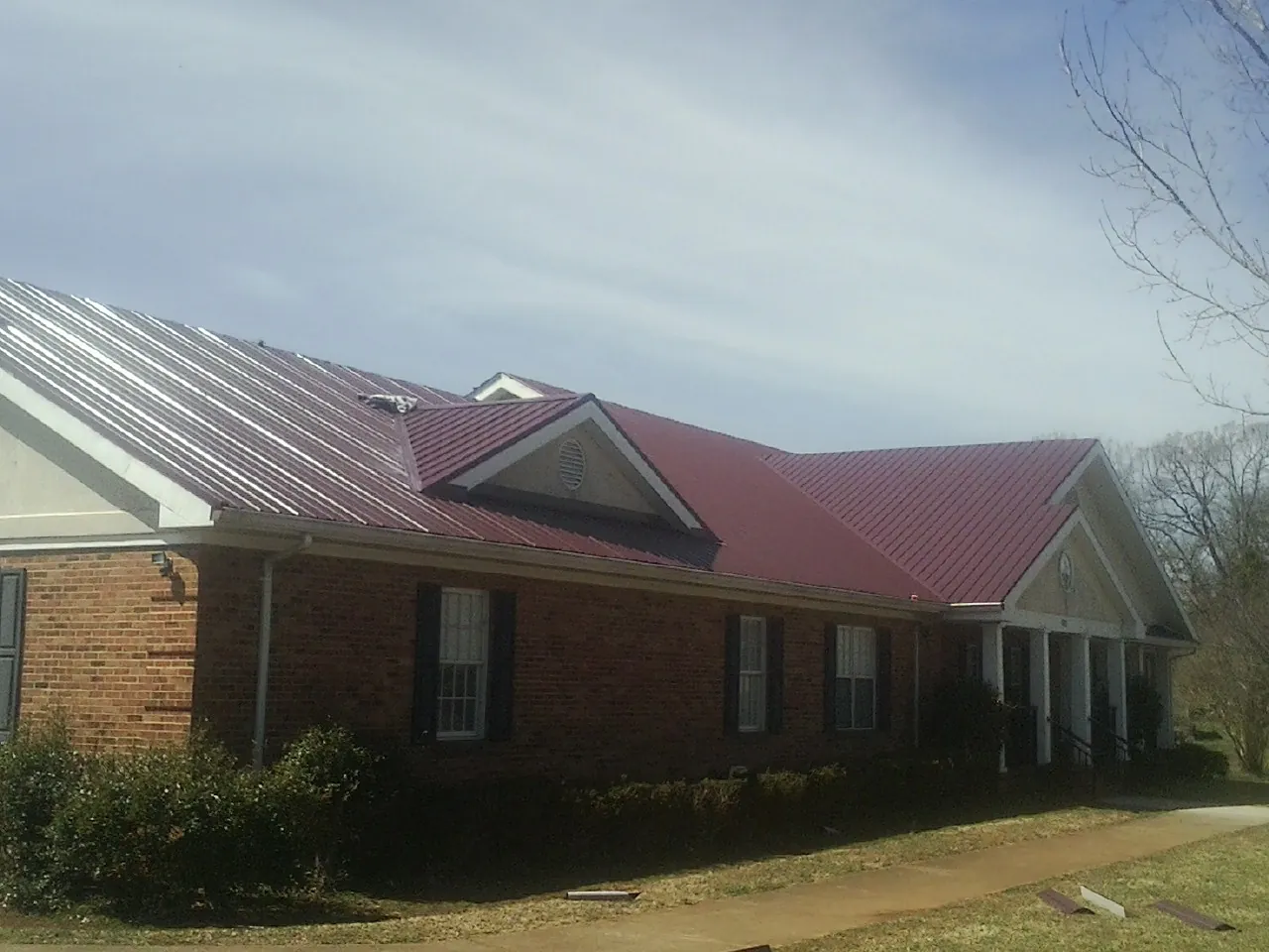Red metal roof with gabled entries on a long brick building, from a Hail Damage Roof Repair job in Mattapoisett
