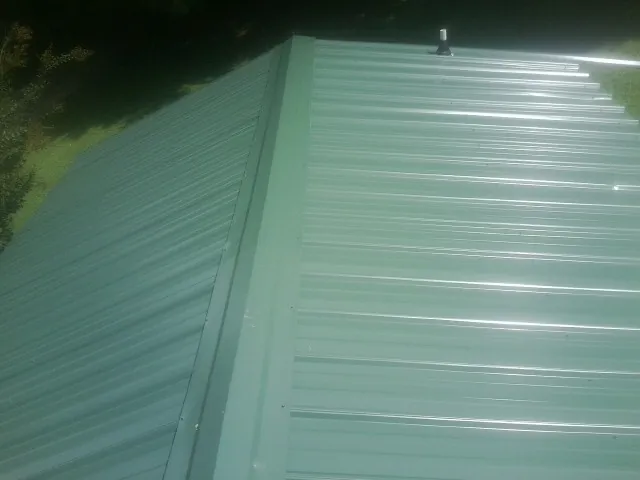 New green metal panels meeting at the ridge of a roof — Flat Roof Repair work by our crew in Mattapoisett
