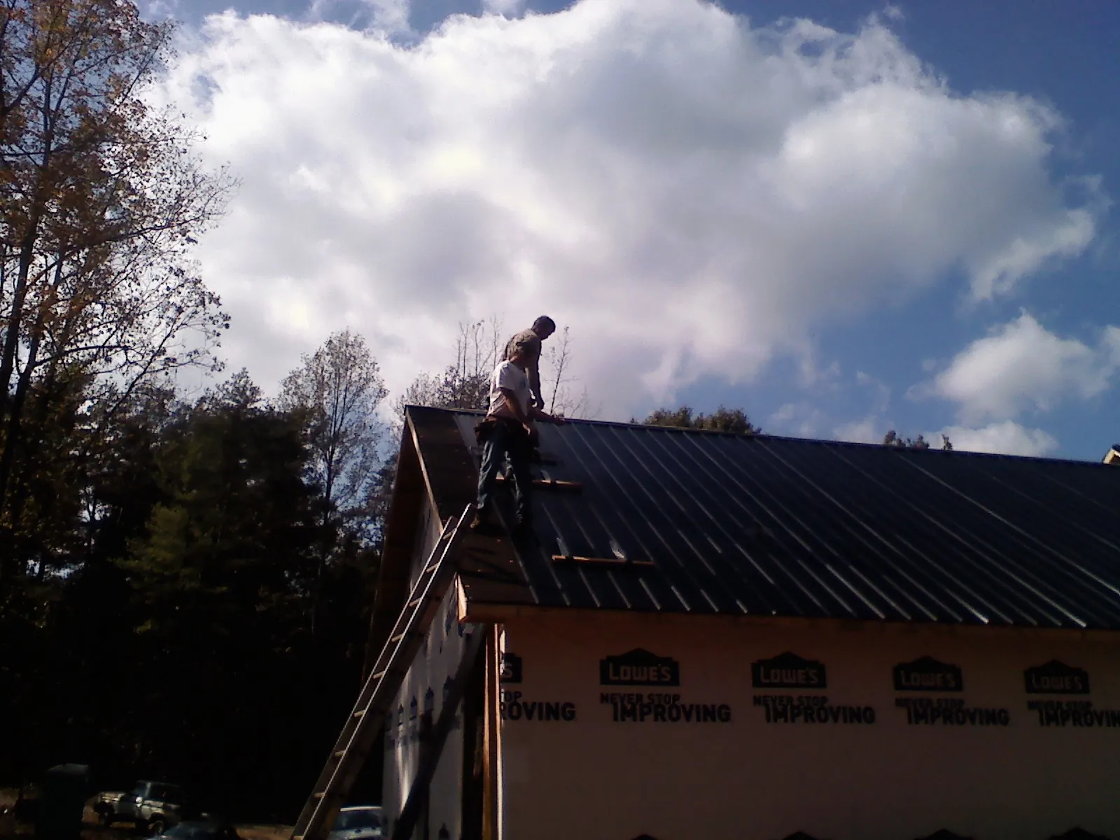 Roofer fastening dark metal panels high against a cloudy sky, from a Roof Inspection job in Mattapoisett