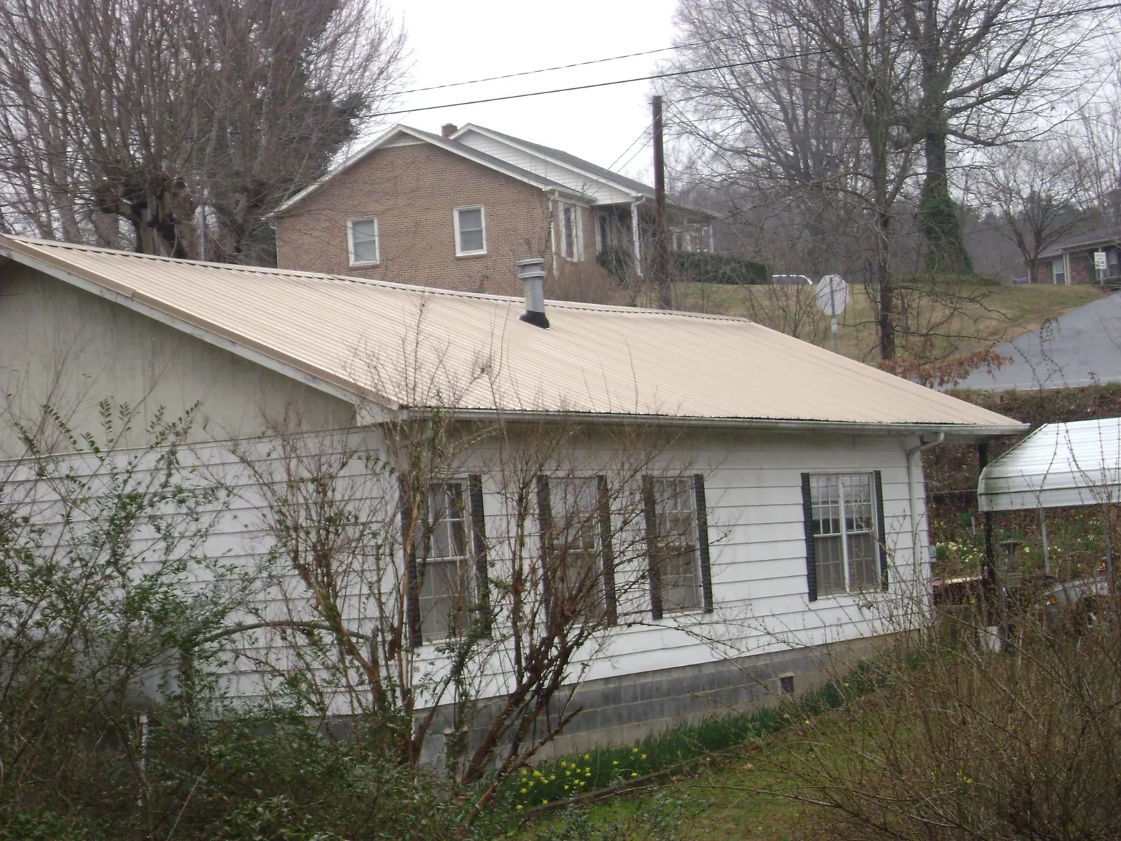 Tan metal roof on a white sided house set into a hillside — Commercial Roofing by Roofing Brothers in Mattapoisett