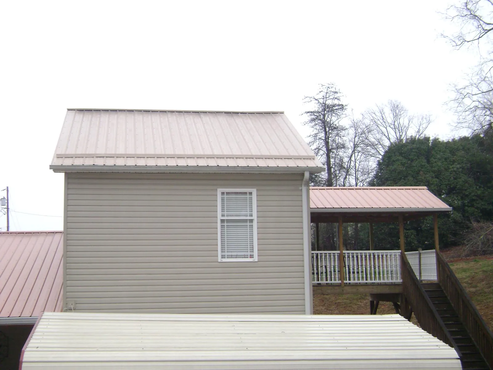 Tan metal roofs on a two story addition and attached porch, from a Roof Replacement job in Mattapoisett