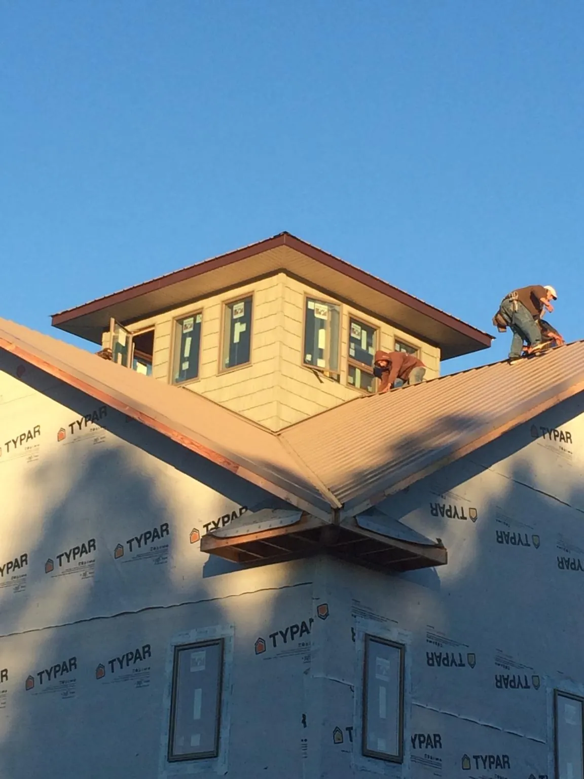 Roofers working around a rooftop cupola on a new metal roof at sunset — Roof Waterproofing in Mattapoisett by Roofing Brothers